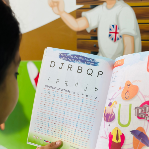 Close-up of a child holding the Kenbee Alphabet Part-D book, displaying an educational activity page to match capital letters with small letters and practice writing Q, D, P, B, R, and J.