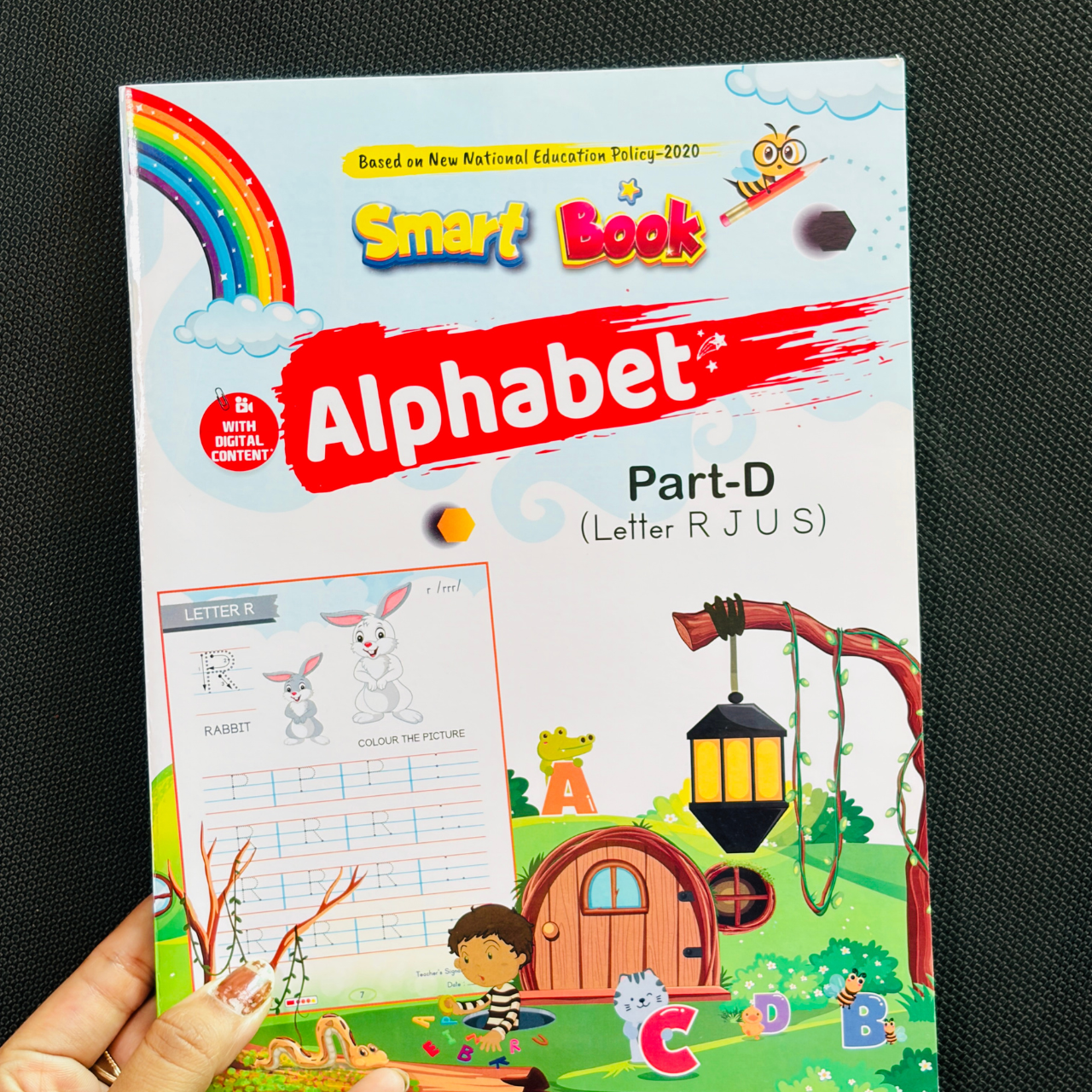 Front cover of Kenbee Smart Book Alphabet Part-D children's workbook, featuring colorful cartoon graphics of a rabbit, fairy-tale house, a rainbow, and a banner highlighting "Letter R J U S" based on NEP 2020.