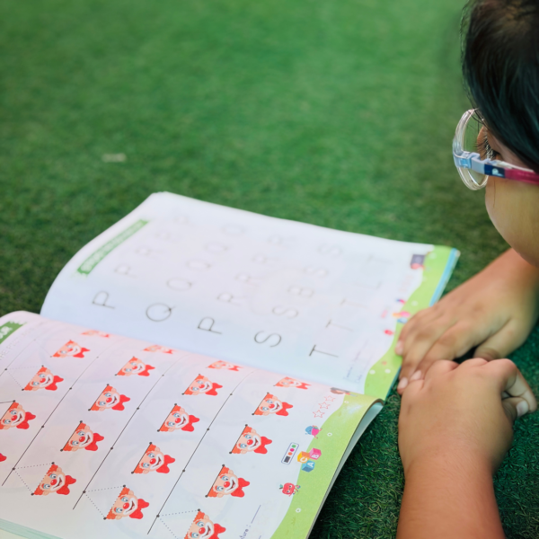 A close-up shot of a child looking at interactive tracing worksheets inside Patterns with Alphabet Part-B Beginner, featuring rows of alphabet letters and playful cartoon clown illustrations.